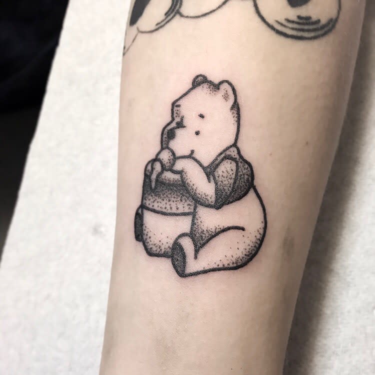 Dotwork tattoo of Winnie the Pooh sitting and enjoying honey from a pot on a person's forearm